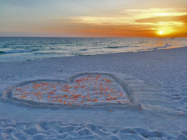 Heart in sand with rose petals at golden sunset